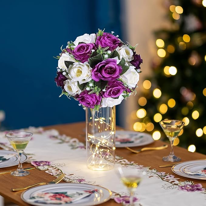 Decorative table setting with a bouquet of purple and white flowers in a vase, surrounded by plates and glasses on a festive background.