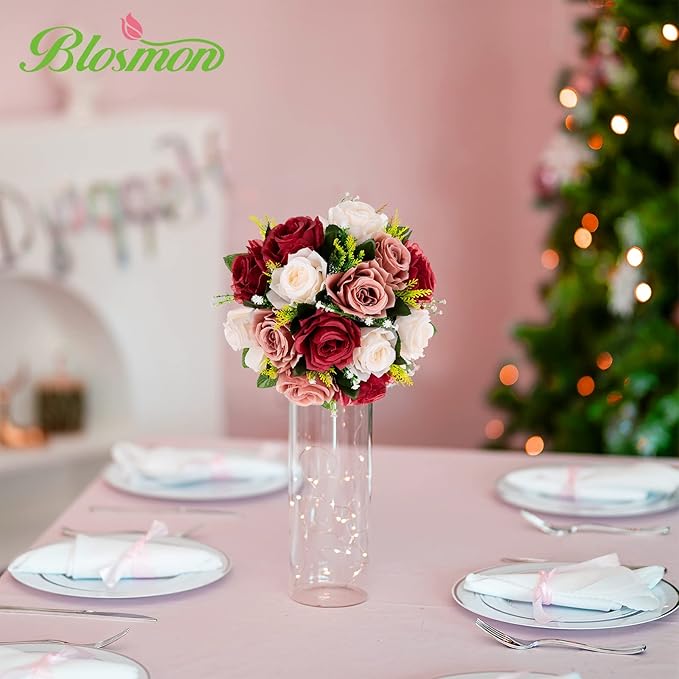 Decorative floral arrangement in a tall vase on a table with a Christmas tree in the background.