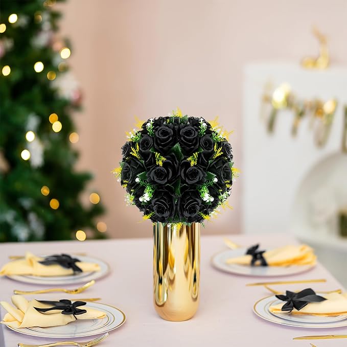 Decorative table setting with black roses in a gold vase, plates with napkins, and a blurred Christmas tree in the background.